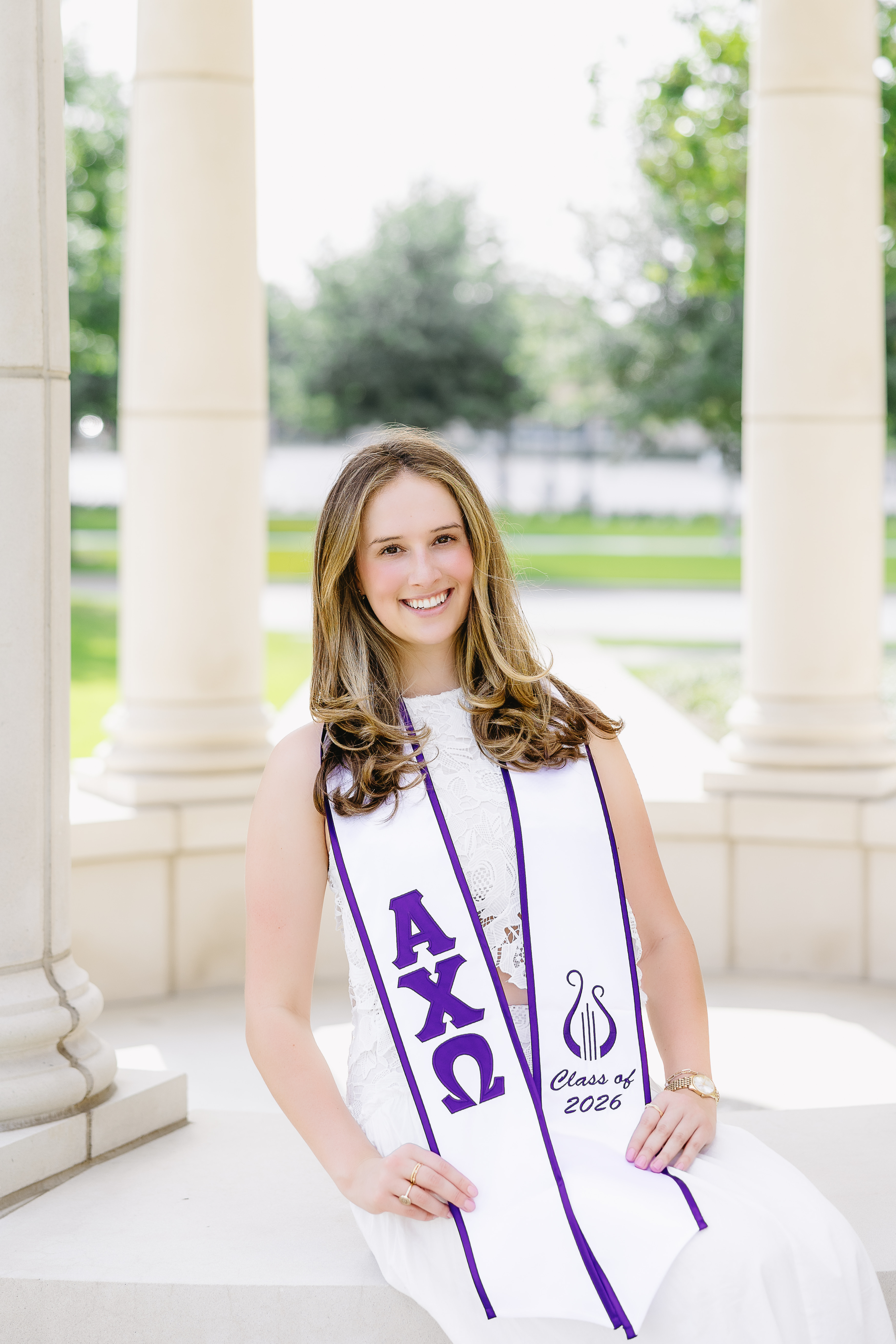 Michel Graham '26 poses on TCU campus for graduation pictures, wearing a white dress and a white sash