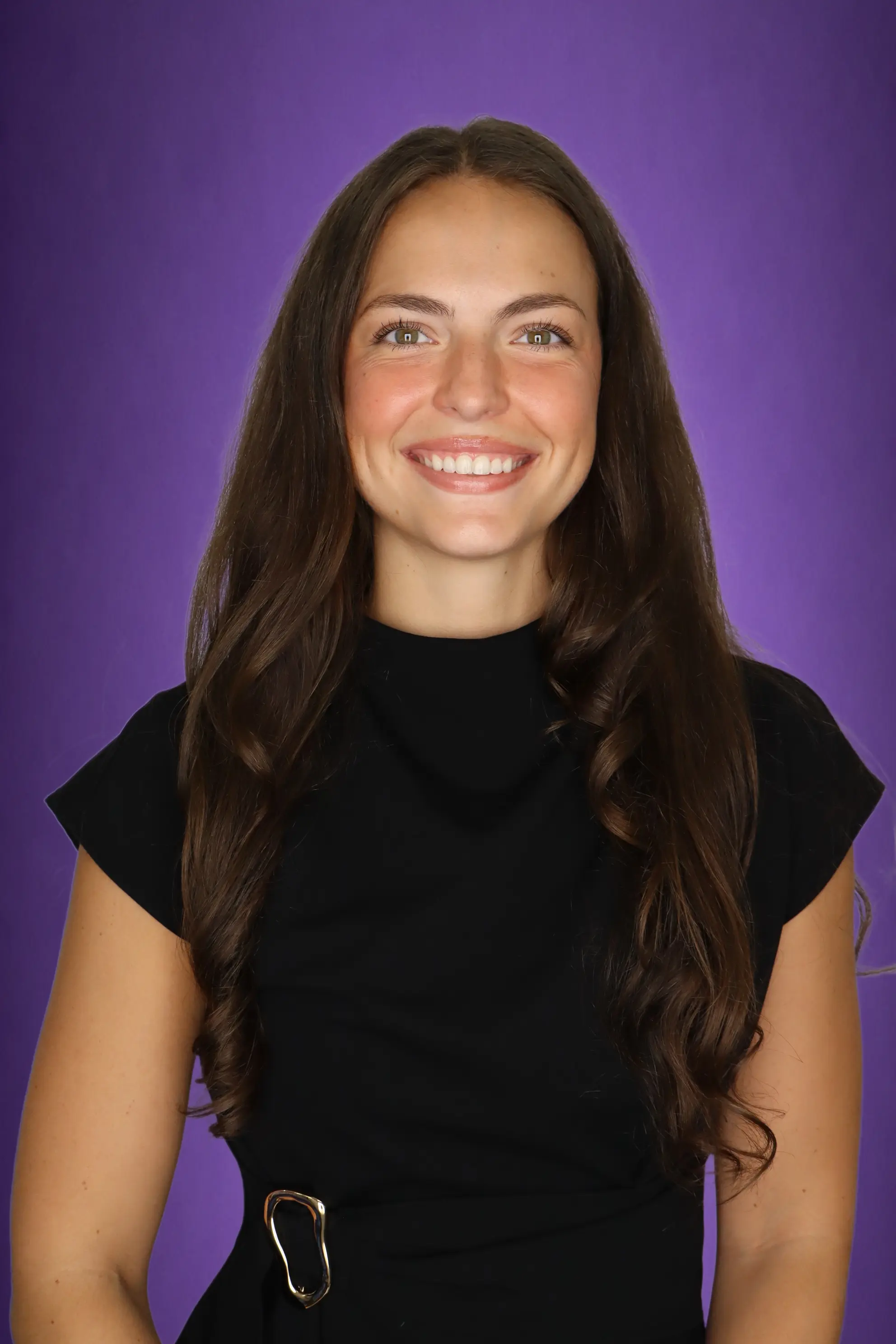 A woman smiling, wearing a black dress, with a purple background