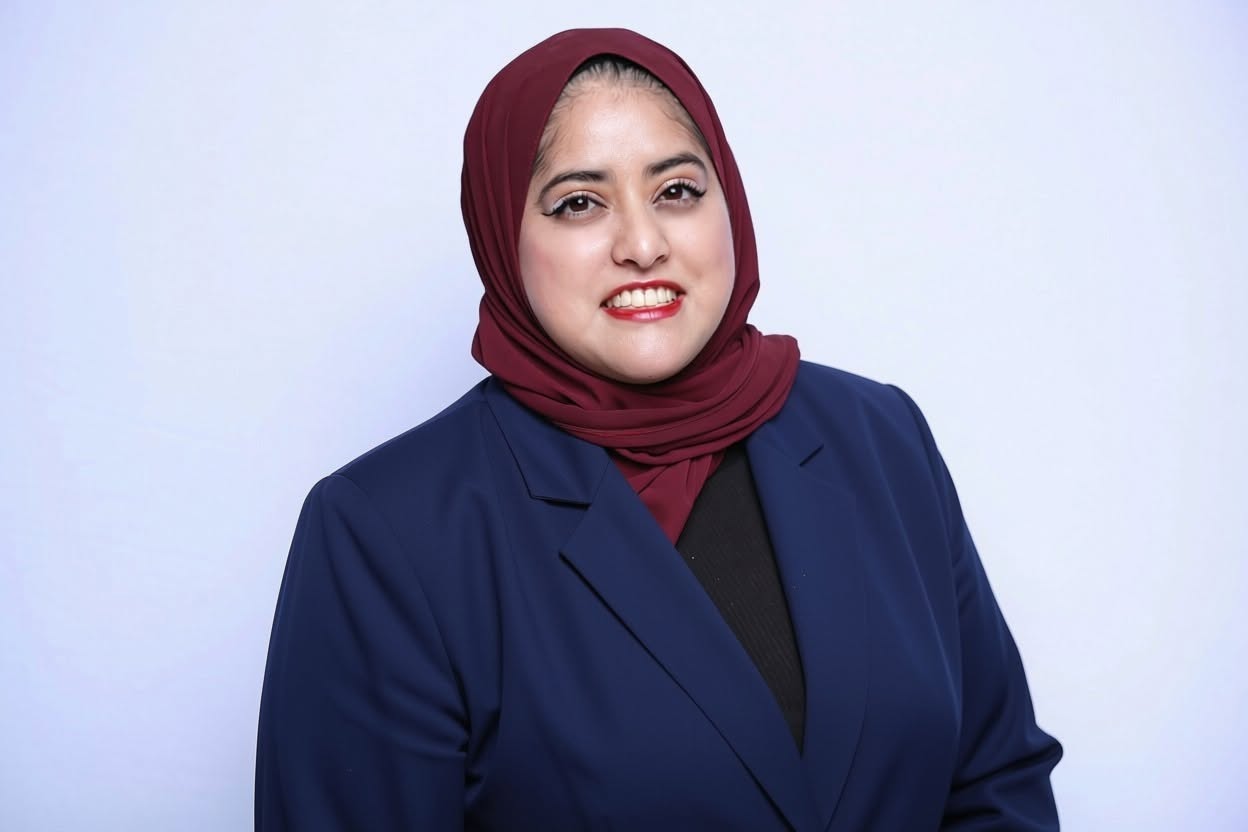 Photo of Kamilah Yang. She is wearing a black shirt with a navy blue blazer and a burgundy headscarf. 