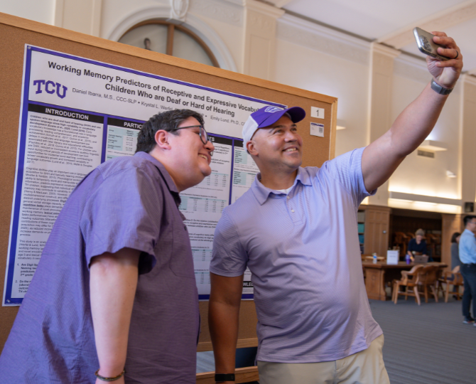 Harris College COSD Ph.D student Daniel Ibarra (left) and a gentleman take a selfie in front of a research poster.
